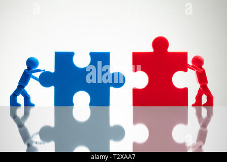 Side View Of Two Miniature Human Figures Solving Jigsaw Puzzles On White Background Stock Photo