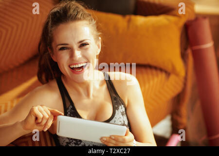 Portrait of happy active woman in fitness clothes at modern home using online personal fitness trainer service in tablet PC. Stock Photo