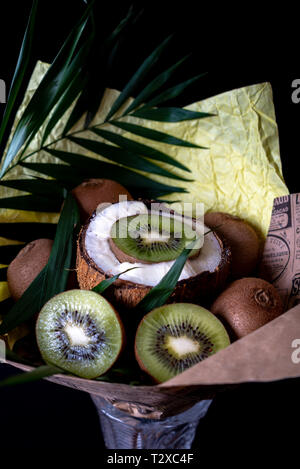 Unique festive bouquet of coconut, kiwi and palm twigs on a black background. Vegetable bouquet. Fruits and Vegetables of the Healthy Concept. Stock Photo