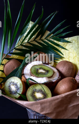 Unique festive bouquet of coconut, kiwi and palm twigs on a black background. Vegetable bouquet. Fruits and Vegetables of the Healthy Concept. Stock Photo