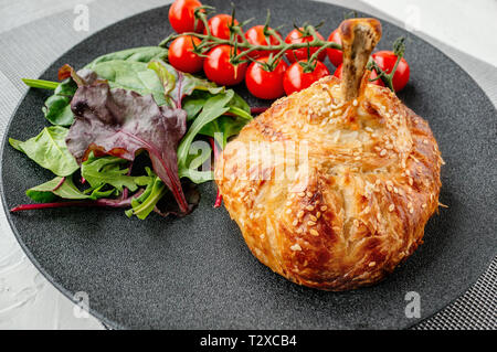 Chicken drumstick in dough baked in the oven with potatoes, tomatoes, onions and spices with a side dish of tomatoes and green salad. Stock Photo