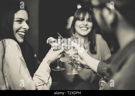 Happy young friends toasting and cheering cocktails at disco bar - Multiracial people having fun enjoying drinks at club - Black and white editing Stock Photo