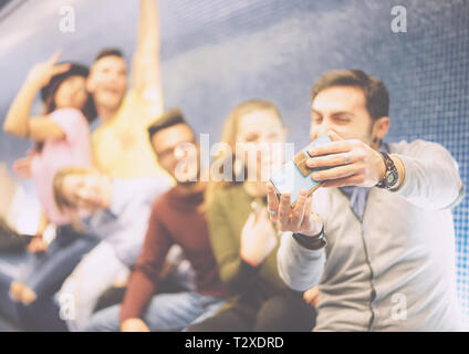 Happy friends taking a photo selfie using their mobile smartphone camera sitting in a underground - Group of multiracial people taking pictures Stock Photo
