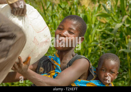 woman with baby on her back collecting bag of maize as relief Stock Photo