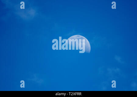 A half moon in the daytime sky with a diagonal pattern of wispy clouds. Stock Photo