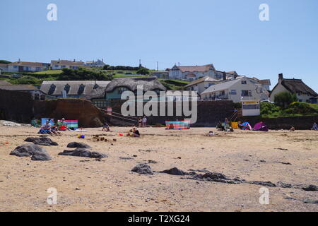 Hope Cove Fishing Village beyond Holiday Makers on the Sandy Beach. South Hams, Devon, UK. Stock Photo