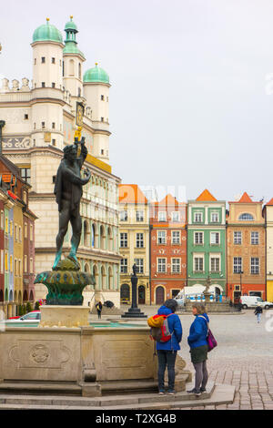 Two women standing talking and chatting by a fountain and statue in the old market square in the polish town of Poznan Poland Stock Photo