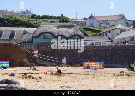 Hope Cove Fishing Village beyond Holiday Makers on the Sandy Beach. South Hams, Devon, UK. Stock Photo