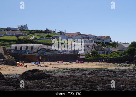 Hope Cove Fishing Village beyond Holiday Makers on the Sandy Beach. South Hams, Devon, UK. Stock Photo