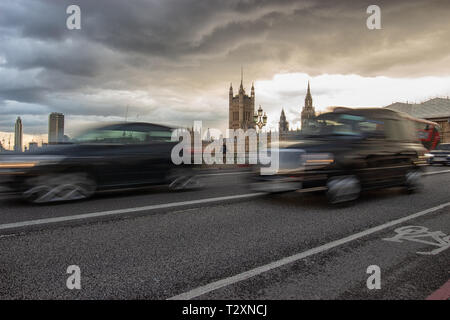 Westminster, London, England, April 3 2019. A famous black taxi and other traffic crossing Westminster Bridge with the Houses Of Parliament in the bac Stock Photo