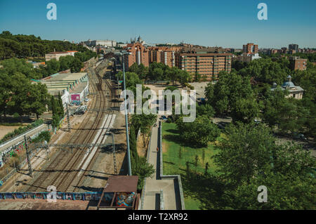 Train station with long rails among buildings and wooden gardens in Madrid. Capital of Spain with vibrant and intense cultural life. Stock Photo