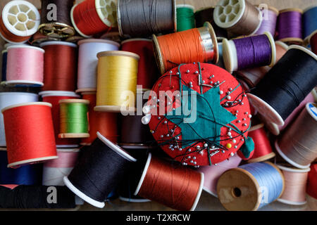 A tomato pin cushion with spools of colorful thread in a sewing kit. Stock Photo
