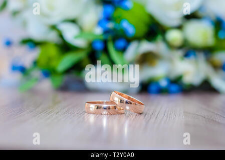 Beautiful gold wedding rings on the table next to the bride's bouquet of white and blue flowers Stock Photo