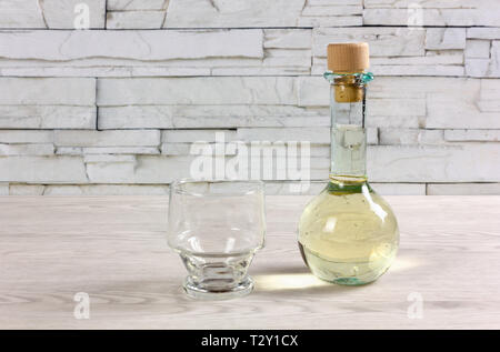 A small bottle on a wooden table, closed by a cork, full of white wine and next to an empty glass Stock Photo