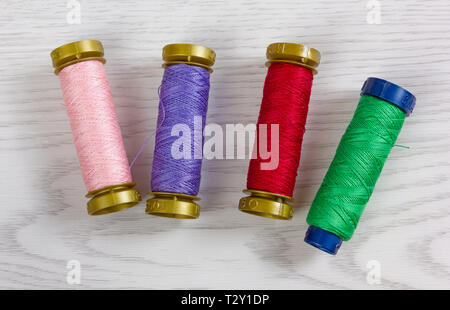 Four thread spools of different colours on a white wooden background Stock Photo