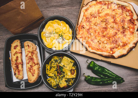 Top view. Take away italian pasta food. Pizza with box green peppers, garlic bread, fetuccine and ravioli on plastic box. Fast italian food at home Stock Photo