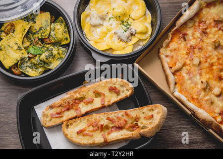 Take away italian pasta food. Pizza with box green peppers, garlic bread, fetuccine and ravioli on plastic box. Fast italian food at home Stock Photo