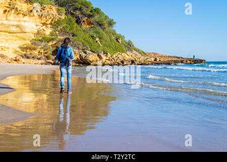 back view of young woman with backpack walking on the beach Stock Photo