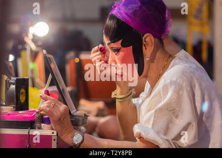 Actress from a Chinese opera group painting mask and putting makeup on her face before the cultural drama and musical performance at the backstage in  Stock Photo