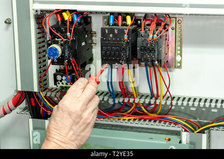 Electricial engineer tightening connections on a contactor in a control panel Stock Photo