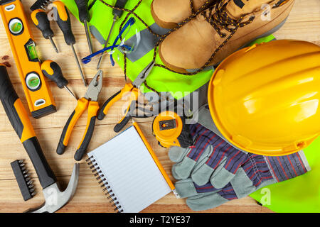 High visibility vest with work boots and yellow hard hat along side various hand tools on a work bench Stock Photo