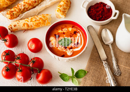 Tomato Soup with Basil, Red Paprika, Whipping Cream, and Garlic and Cheese  Bread Sticks, White Background Stock Photo