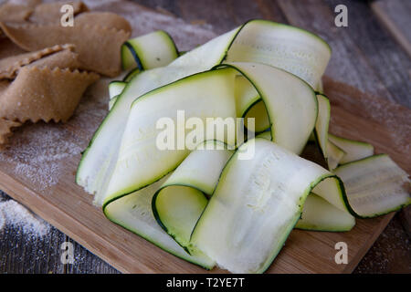 Fresh cut zucchini ribbons on cutting board with homemade pappardell pasta in background. Stock Photo