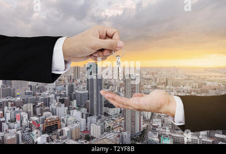 Real estate business, residential rental and investment. Businessman handover keys, with city sunrise background Stock Photo