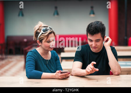 Woman and young man talking together and using mobile phones sitting by a table in cafe Stock Photo