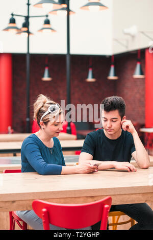 Woman and young man talking together and using mobile phones sitting by a table in cafe Stock Photo