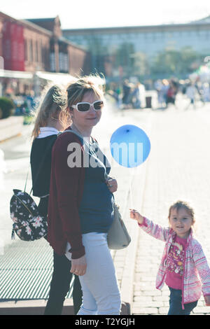 Mother walking with her daughters, spending time in center of city outdoors. Little girl holding blue balloon Stock Photo