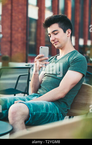 Young man having fun with smartphone, capturing photo, sitting in center of town Stock Photo