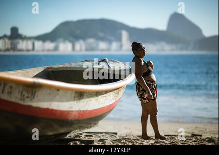 RIO DE JANEIRO - FEBRUARY 10, 2017: A Brazilian woman leans against a traditional wooden boat on the shore of Copacabana Beach. Stock Photo