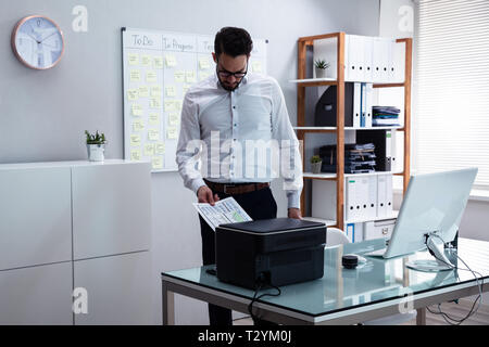 Photo Of Young Businessman Using Printer In Office Stock Photo