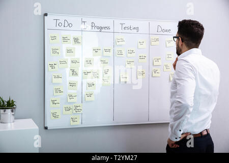 Rear View Of Businessman Looking At Adhesive Notes On White Board Stock Photo