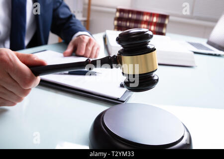 Midsection Of Male Judge In Courtroom Striking Mallet On Sound Block Over Desk Stock Photo