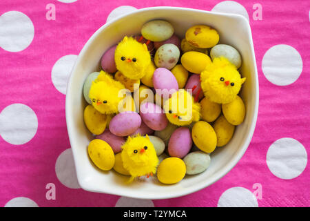 speckled egglets and fluffy chicks in bowl on pink and white polka dots - solid milk chocolate mini eggs with a speckled candy shell ready for Easter Stock Photo