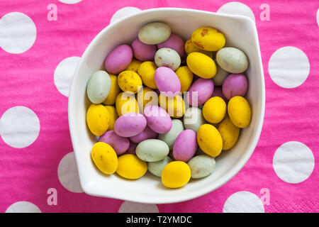 speckled egglets in bowl on pink and white polka dots background - solid milk chocolate mini eggs with a speckled candy shell ready for Easter Stock Photo