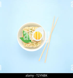 Creative food diet healthy eating concept photo of tasty ramen noodle pasta with egg greens chopsticks and bowl on blue background. Stock Photo