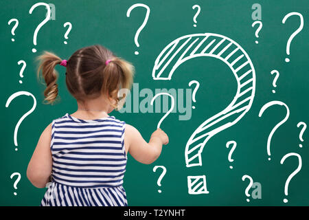 Rear View Of Little Girl Writing Question Marks On Chalkboard Stock Photo