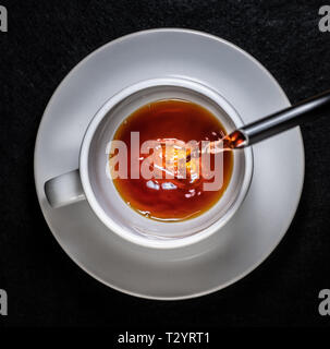Coffee and cream pouring into a white cup on a white saucer with a black background Stock Photo