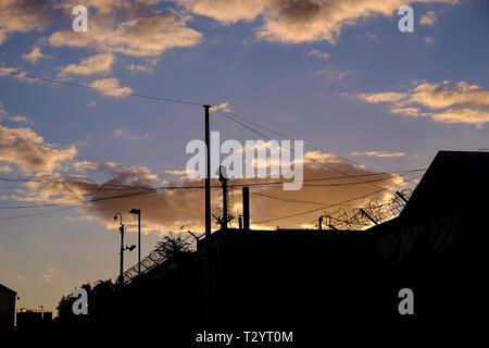Barbed wire ad surveillance camera silhouetted against twilight clouds in an industrial area of Sheffield Stock Photo