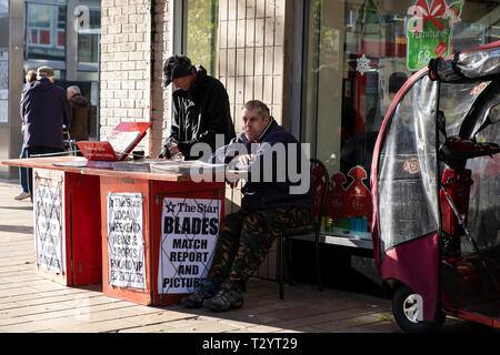 Two men working on a Sheffield Star local newspaper stand on a city street in Winter Stock Photo