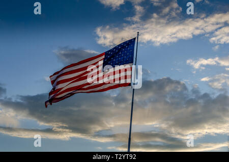 The Flag of the United States of America flying on a pole in a cloudy blue sky. Let freedom ring with the stars and stripes. Stock Photo