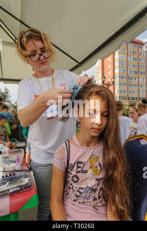 Tyumen, Russia - August 26, 2016: Open Day of Sberbank for children. Young woman hairdresser do hairstyle girl in beauty point Stock Photo