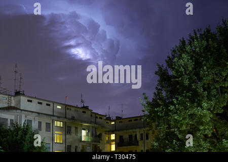 Buildings and green trees at night, illuminated sky during a lightning storm Stock Photo