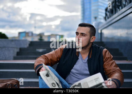 portrait of young guy in  leather jacket reading newspaper in the city. the man thoughtfully looks away Stock Photo