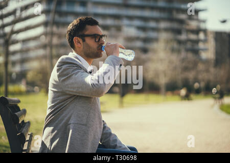 Young businessman is resting and drinking water in park after work. Stock Photo