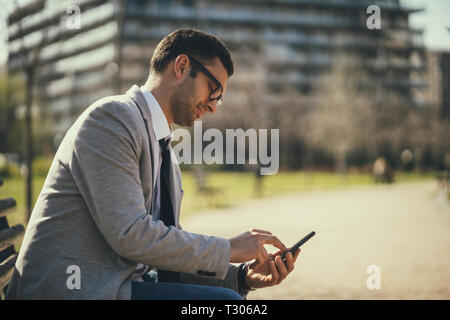 Young businessman is using smartphone in park. Stock Photo