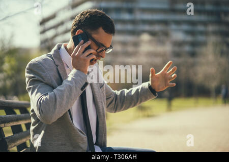 Young businessman is talking on phone in park. Stock Photo